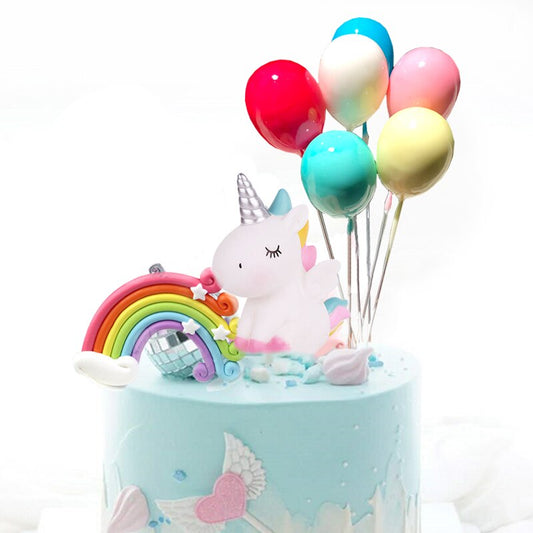 Décoration licorne pour gâteau comprenant 6 petits ballons, une licorne miniature et un arc-en-ciel.