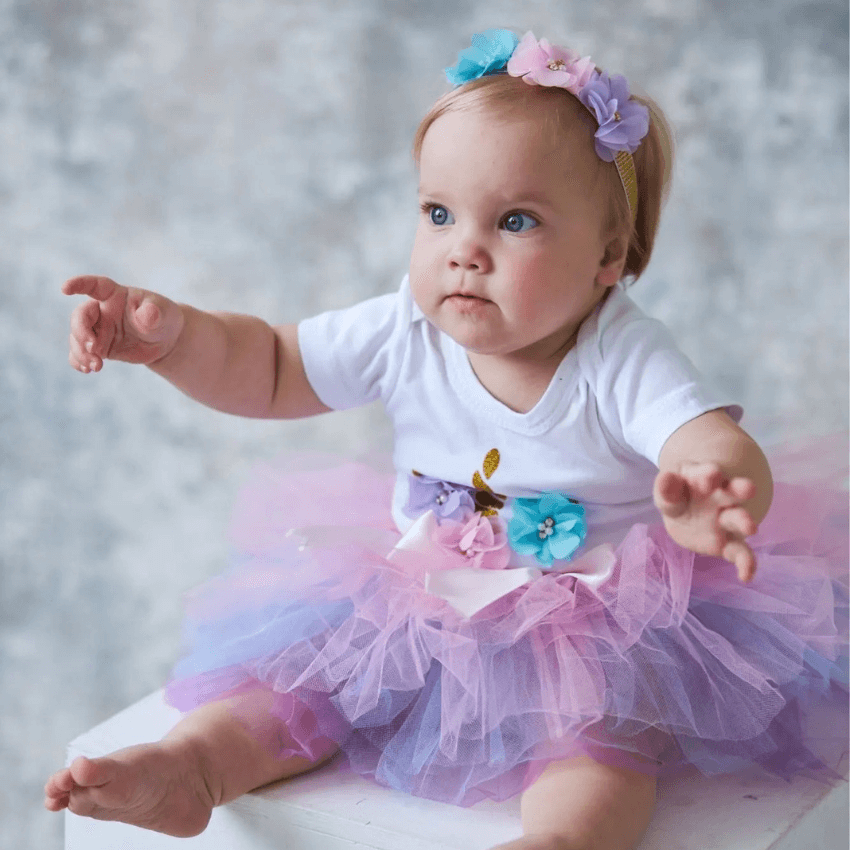 Bébé fille qui porte un deguisement licorne body tutu anniversaire violet bleu et rose premier anniversaire