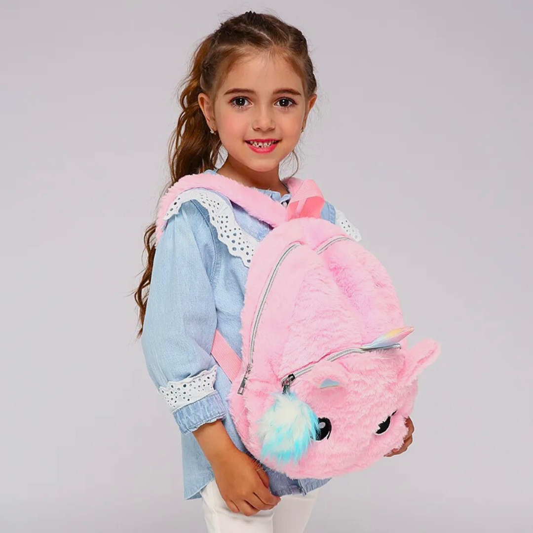 Petite fille qui porte un sac a dos licorne tout doux rose avec pompon